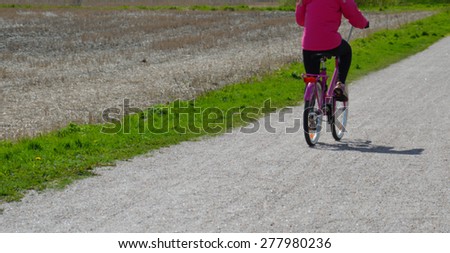 Young girl riding her bike in the countryside - slightly blurred image. Lonely girl. Young female cyclist. Sandy road. Bright colorful clothes.