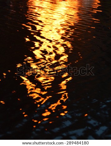 Flames of a bonfire reflecting in the surface of a lake. Idyllic photo of fire mirrored on the water. Reflection of scintillating fire sparkles. Motion blur.