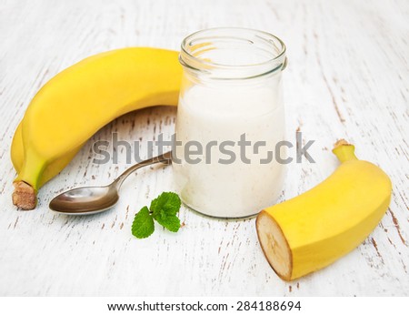 Banana yogurt and fresh bananas on a wooden background