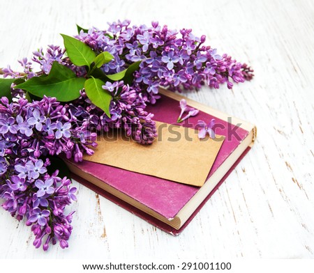 Lilac flowers and old book with card on a wooden background