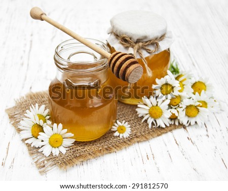 Jars of honey with camomile on a old wooden background