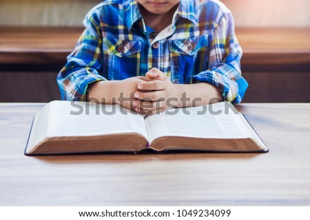 A child praying on open bible with blurred page on wooden table
