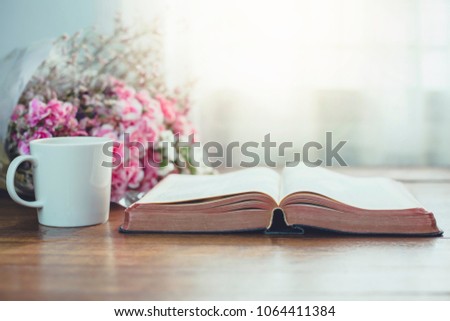 Holy bible with a cup of coffee and  flowers on wooden table against window light, Christian background with copy space