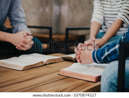 group of christianity  sitting around wooden table with open blurred bible page and praying to God together