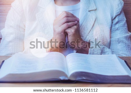 close up of woman hands praying to God while reading bible on wooden table  in morning devotion, Christian