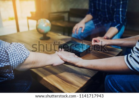 Christian friends holding hands together surrounded wooden table with blurred bible and world globe, christian prayer for world mission concept