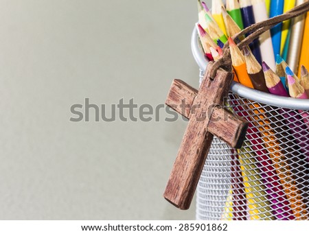 image of the wooden cross and colors pencils in white basket