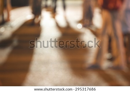 people standing on concrete  ground  while watching concert  with shadows from the concert and a night light  in the city, abstract blurred background