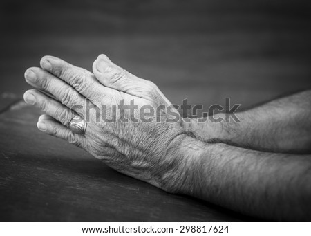 praying hands of the old  man on wooden background, black and white