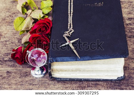 The metal  cross  over the  old bible with world globe model and  red roses on wooden background, world mission concept.