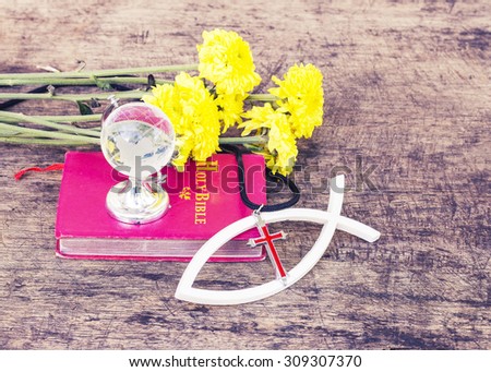 The red cross  over the white christian fish and the world globe model on the red bible yellow flowers on wooden background, world mission concept.