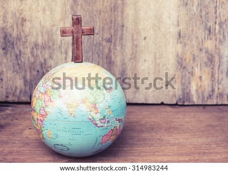 The wooden cross on top of the world globe on wooden background with copy space, world mission concept
