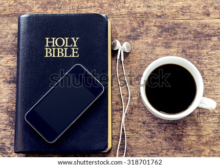 smartphone over the holy bible with black coffee cup on wooden background, vintage color