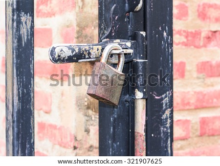 A  padlock on a black metal  gate with red bricks pole as a background