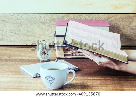 woman hand holding and reading bible  with  a cup of coffee and some books,  clock on the wooden table