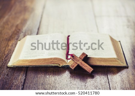 the wooden cross over opened bible on wooden table with window light, vintage tone