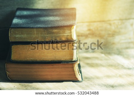 stack of old bible on wooden background with widow light, vintage tone and light effect, copy space