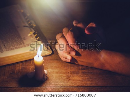 praying hand  and blurred open bible on wooden table with candle light and the light from above, trust concept , Christian background with copy space for your text