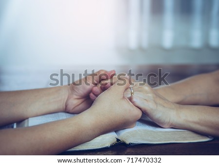 Two  people are praying together over holy bible on wooden table