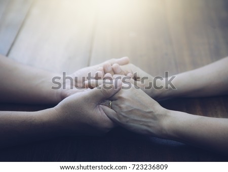 Couple of husband and wife are holding hands and pray together  on wooden table  with the light from above with  copy space for your text