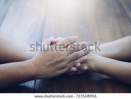 husband and wife join hands and  pray  together on wooden table with the light from above with copy space fro your text.
