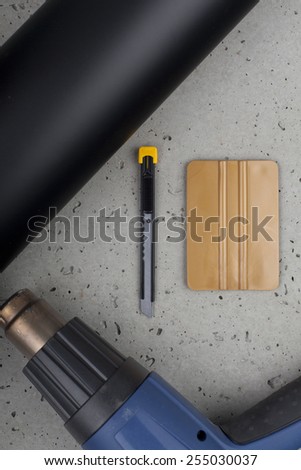gold squeegee, knife, heat gun and black mate vinyl on concrete floor