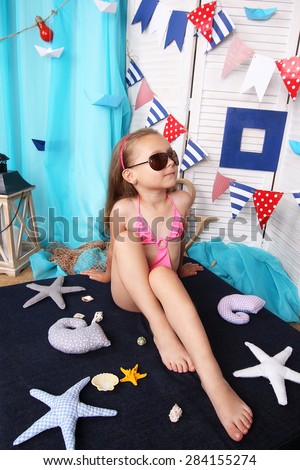 Beautiful little girl in a pink bikini posing on studio shooting with summer scenery.