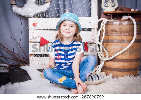 Beautiful girl in a hat sitting barefoot near the barrel, marine networking and cables. Cute little girl smiling on the background of summer sea scenery. Happy and carefree childhood