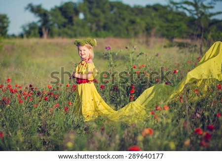 Beautiful little girl in a yellow dress with a long train, with a wreath on his head standing in a field with poppies. Little fairy. Princess fields.