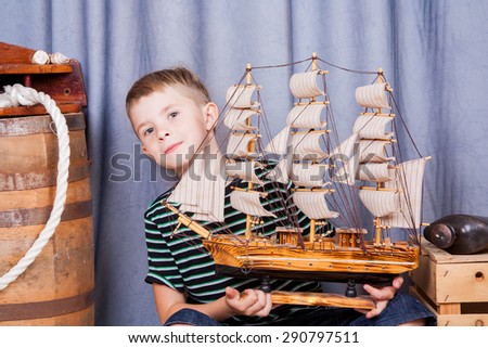 Funny little boy holding a wooden sailboat and parking on the profession of captain. The future is in your hands. Profession comes from a childhood dream
