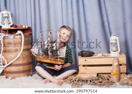 Funny little boy holding a wooden sailboat and parking on the profession of captain. The future is in your hands. Profession comes from a childhood dream