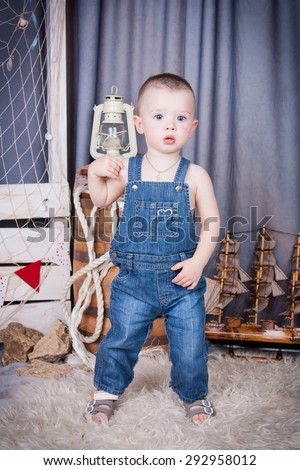 Cute kid with big gray eyes in denim overalls playing among the maritime decor.Handsome boy looking curiously into the frame.Handsome boy looking curiously into the frame.