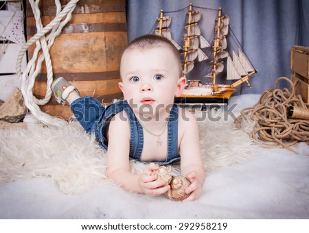 Cute kid with big gray eyes in denim overalls playing among the maritime decor.Handsome boy looking curiously into the frame.Handsome boy looking curiously into the frame. boy lying on the skin