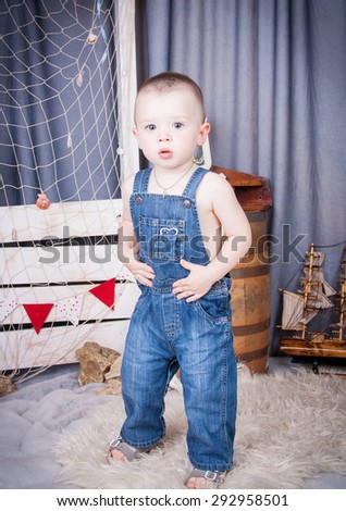 Cute kid with big gray eyes in denim overalls playing among the maritime decor.Handsome boy looking curiously into the frame.