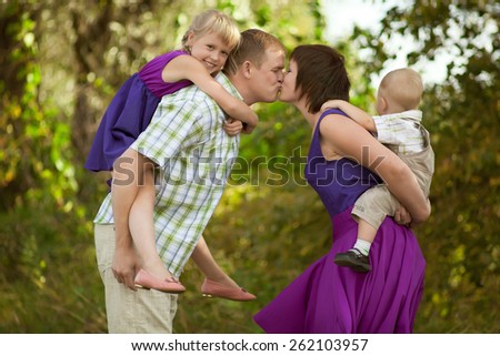 Father, mother, daughter and son walking in the countryside. Parents and children are dressed in the same clothes. Mom and Dad kissing. Children in the hands of parents