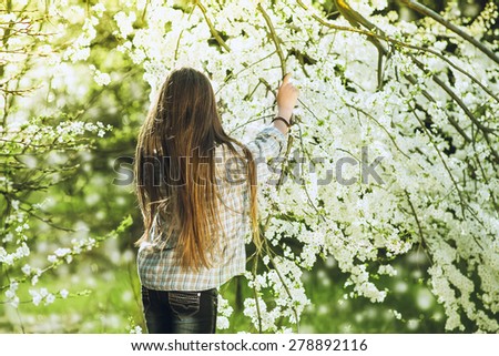 The girl with long hair standing on the background of a flowering tree. She straightens her hair. She is walking in the spring park.