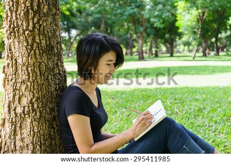 Asian young girl sit to writing letter under the tree in green park