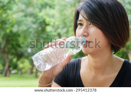 Asian young girl drink water in green park, summer day with drink water bottle
