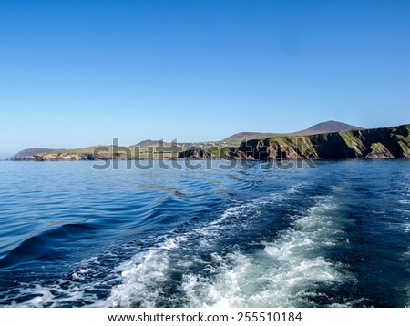 Stern wash from a fishing boat with the Slea Head on the Dingle Peninsula in Ireland with a clear deep blue sky