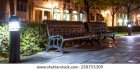 Wooden benches in a pedestrian rest area with floor lamps in Old Montreal at night.