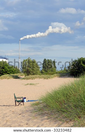 Pollution against to the nature. Chair standing on the beach and the industrial chimney with exhaust smoke in the background