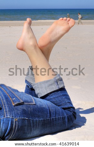 Woman in jeans with crossed legs resting on the beach