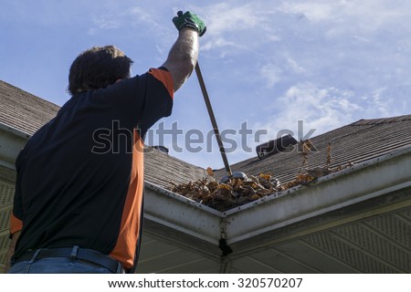 Worker sweeping leaves and sticks from a valley of a roof.