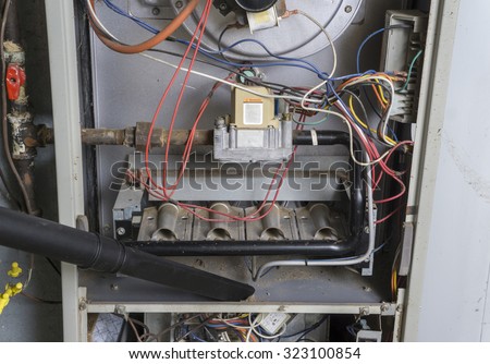 Repairman vacuuming inside of a gas furnace during a cleaning.