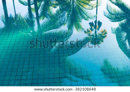 Reflection of coconut trees and sugar palm tree in turquoise color swimming pool