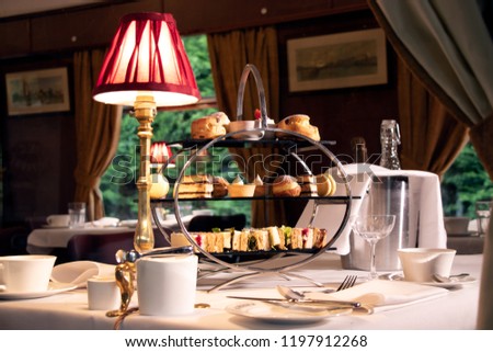 Vintage late afternoon tea stand with sandwiches, cakes and tea as see through the window of a train carriage.