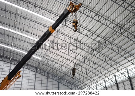 Yellow truck crane boom with hooks in the warehouse.  Indoor lighting. The background is the new roof of warehouse.