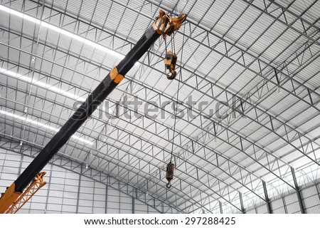 Yellow truck crane boom with hooks in the warehouse.  Indoor lighting. The background is the new roof of warehouse.