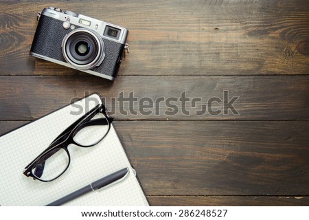Camera, glasses and notepad on wood