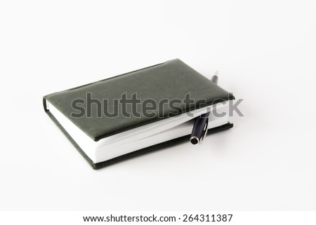 A dark green covered notepad with roller pen isolated